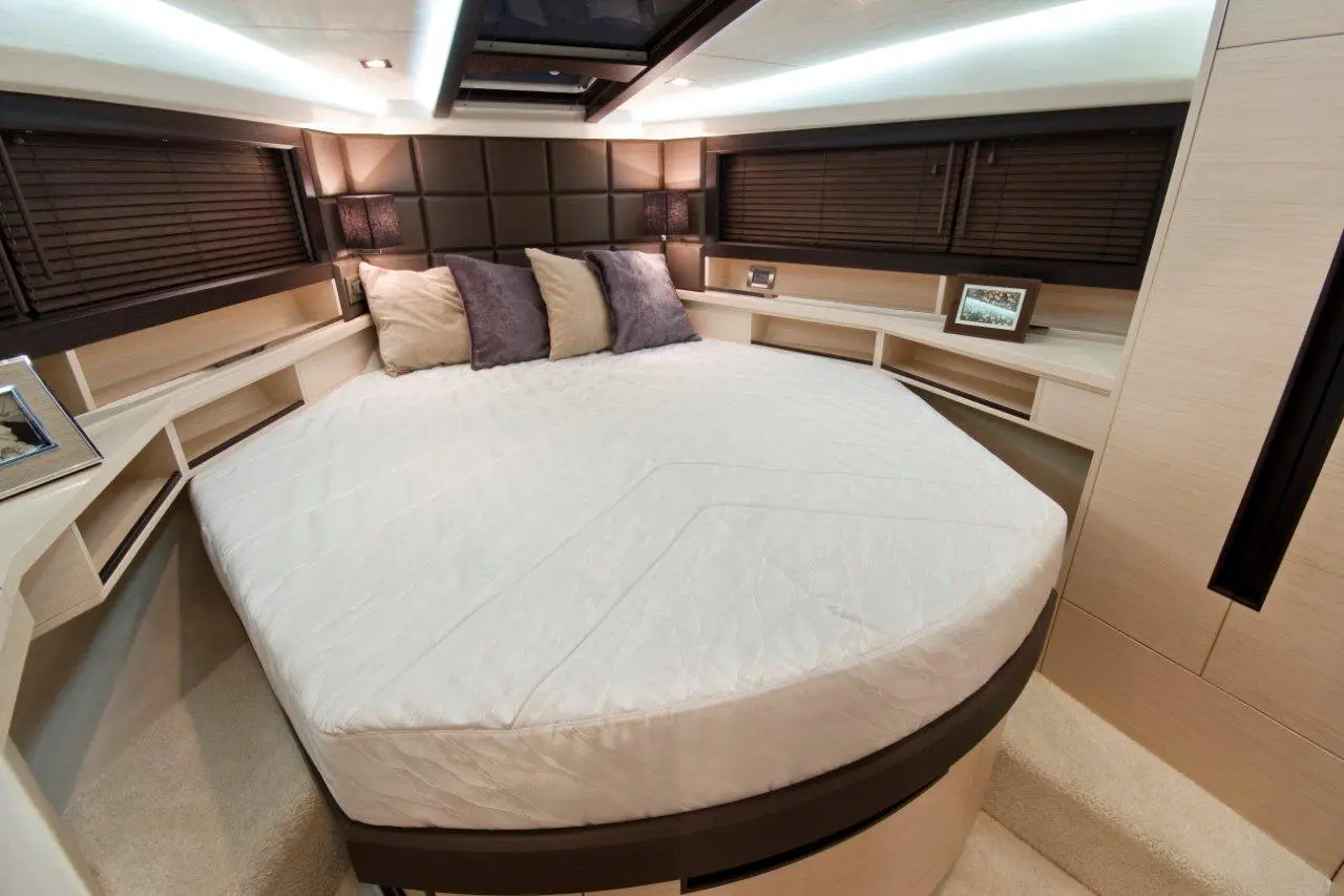 Modern bedroom featuring a round bed, decorative pillows, and stylish lamps against dark wooden panels, with shelves and framed photo.