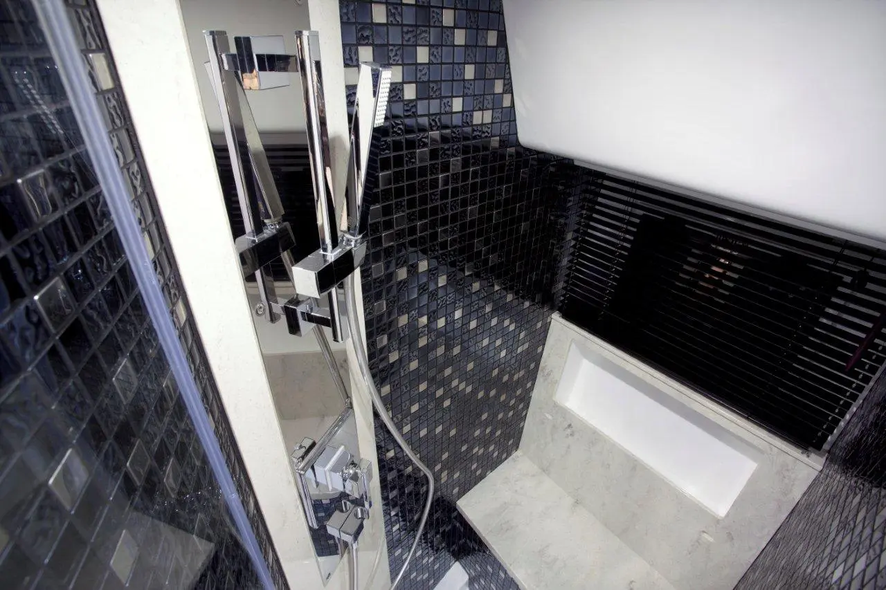 Modern shower space with sleek chrome fixtures, black mosaic tiles, and a marble bench along the wall.