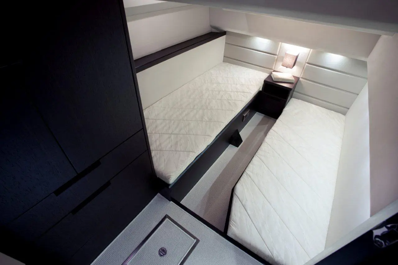 Modern boat cabin featuring two single beds, wooden storage unit, and soft lighting, with beige and dark tones throughout.