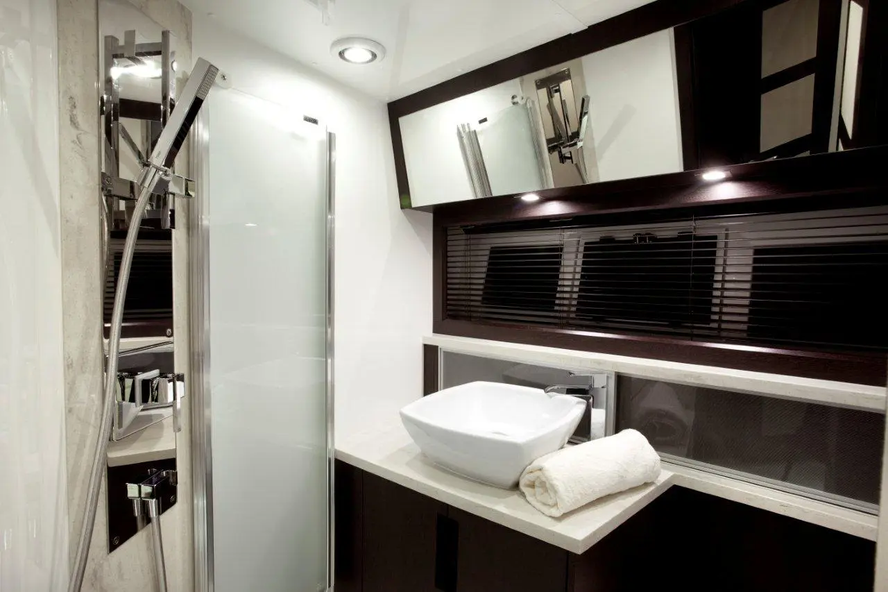 Modern bathroom featuring a shower, a white basin on a countertop, and a neatly arranged towel. Mirrors enhance light.