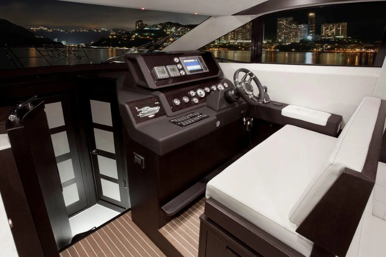 Luxury yacht cockpit showing a modern steering wheel, control panels, and a city skyline at night through large windows.