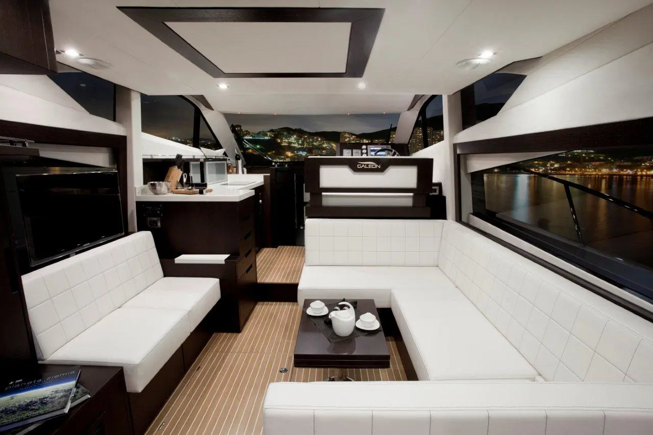 Interior of a luxury yacht featuring modern furnishings, a compact kitchen, and a coffee table with a teapot set.
