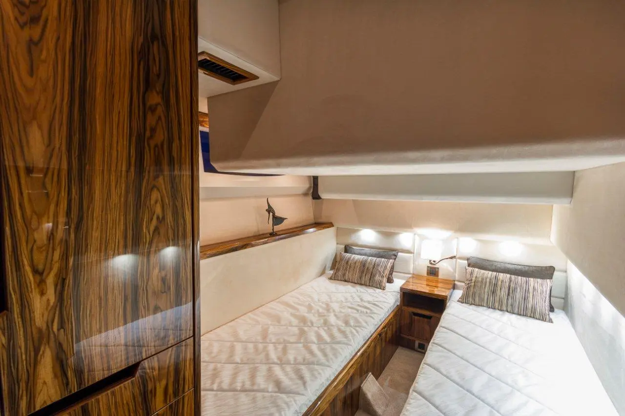 Cozy yacht cabin with two twin beds, wooden accents, reading lights, and a decorative sculpture on a shelf.