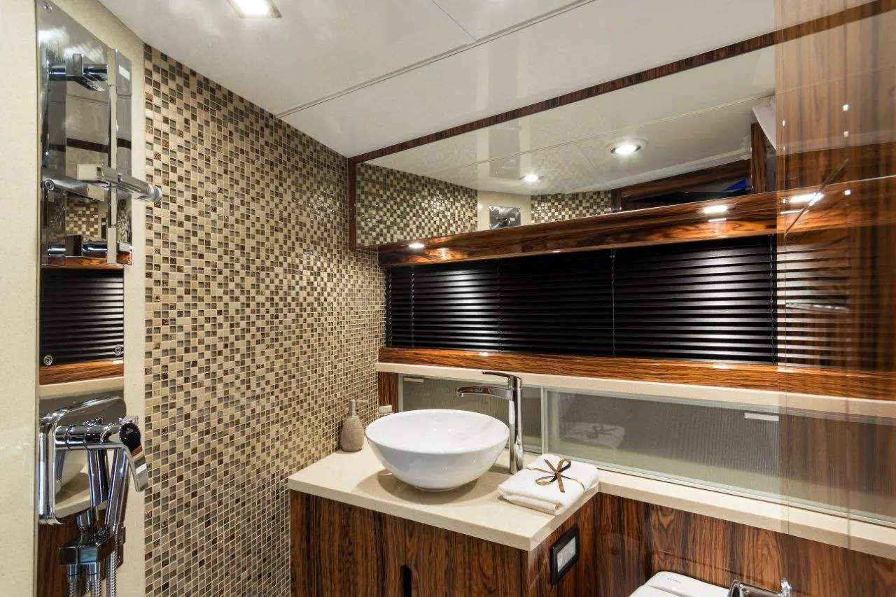 Modern bathroom featuring a mosaic tile wall, elegant sink, wooden cabinetry, and neatly arranged towels.