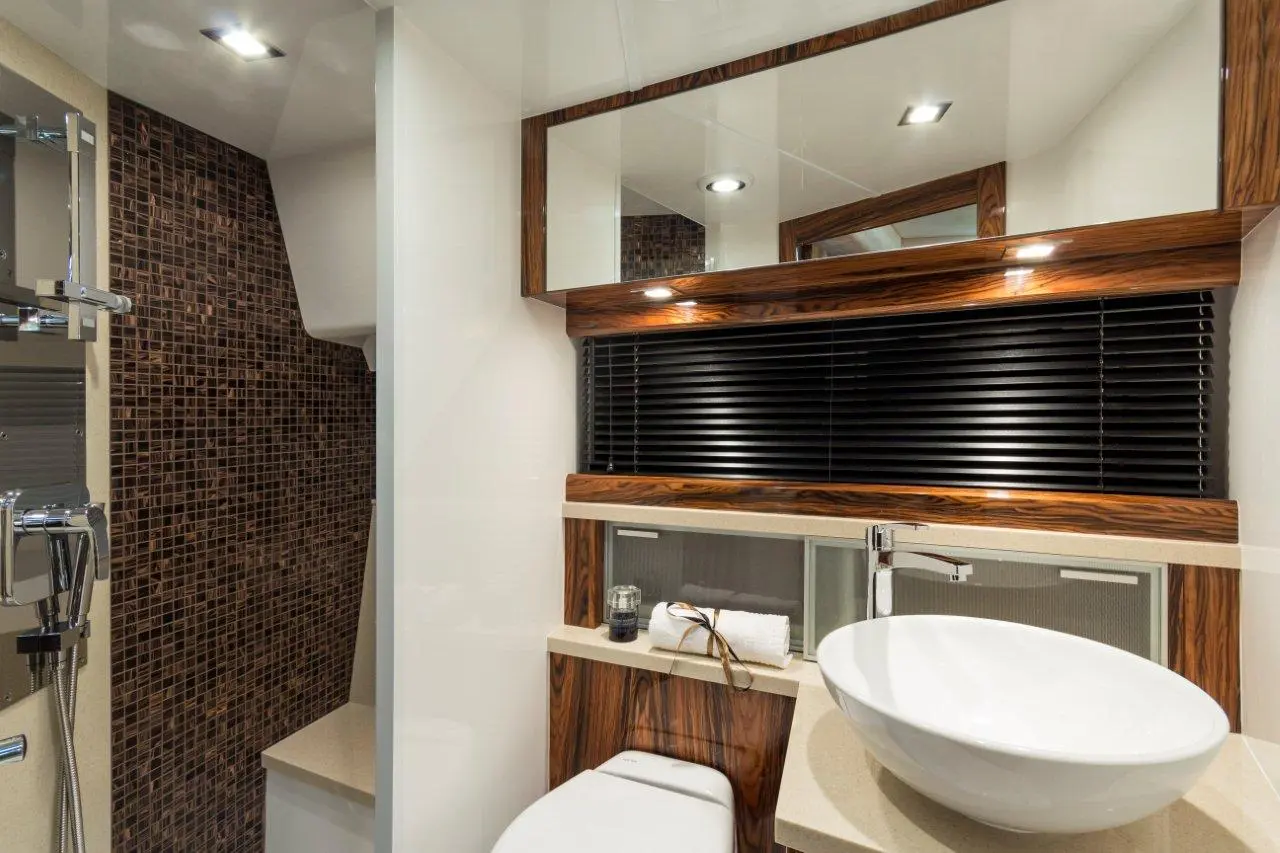 Modern bathroom featuring a round sink, wooden accents, tile wall, and neatly arranged towels with a candle on a counter.