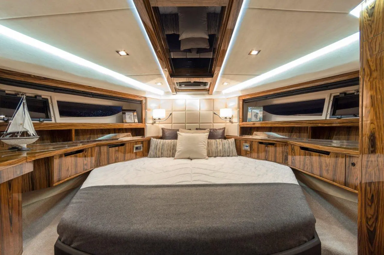 Stylish yacht bedroom featuring a large bed, wooden cabinetry, plush pillows, and a decorative sailboat.