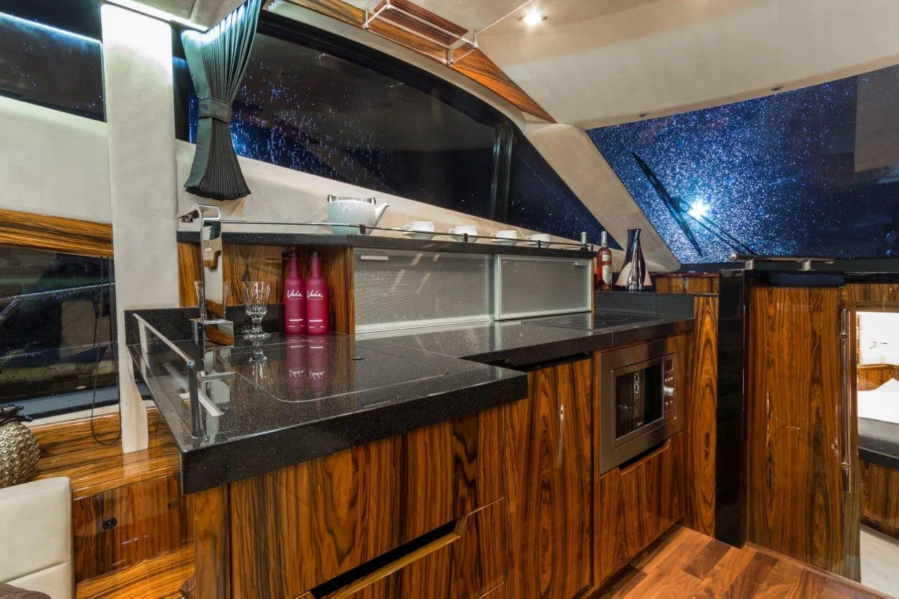 Luxury kitchen area on a yacht featuring wooden cabinets, a black countertop, a kettle, and illuminated glassware.