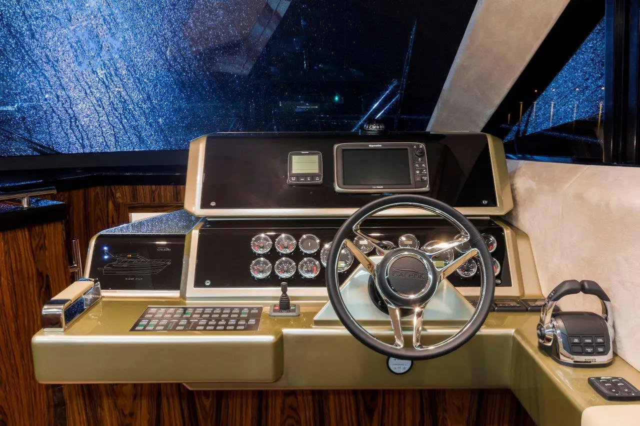 Luxurious yacht control panel featuring a steering wheel, gauges, digital screen, and rain-splattered windows.