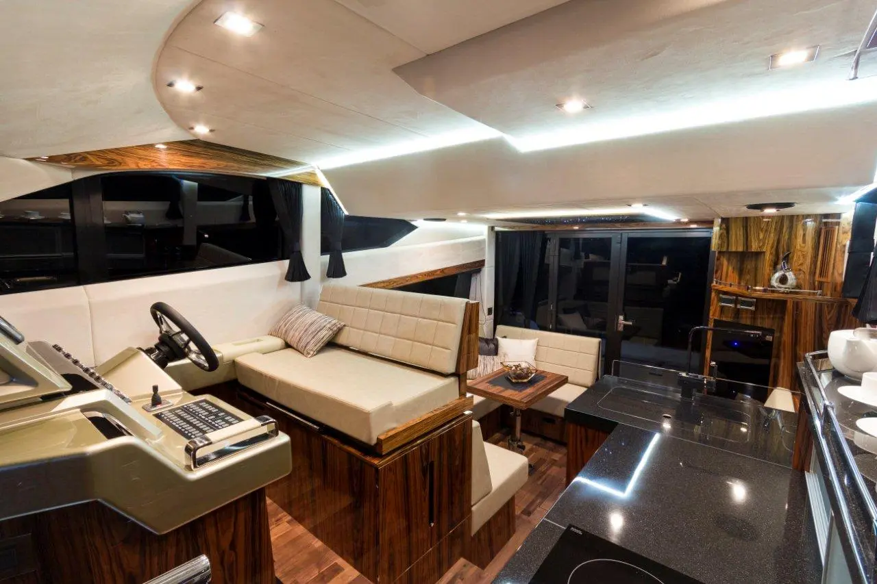 Modern yacht interior featuring a steering wheel, seating area, kitchen counter, and large windows with a stylish design.