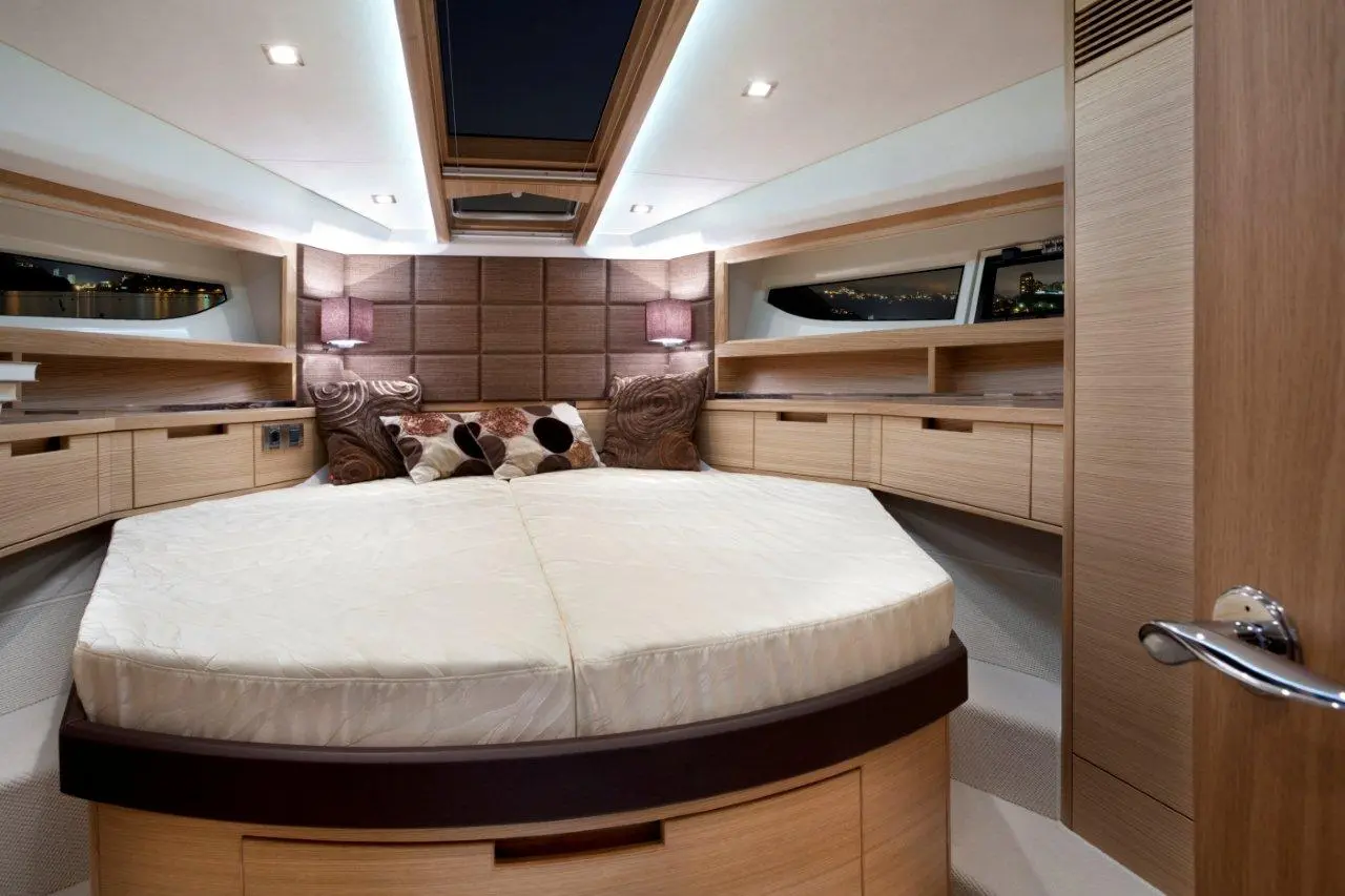 Modern boat cabin featuring a round bed, stylish decor, and ambient lighting, with a view through a large window.