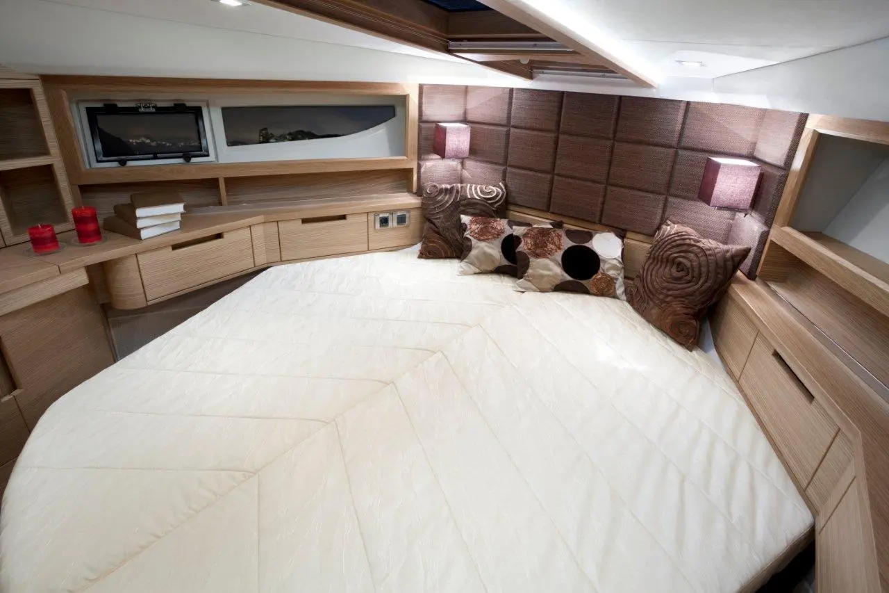 Stylish boat cabin with a large bed, decorative pillows, storage drawers, and soft lighting, showcasing modern interior design.