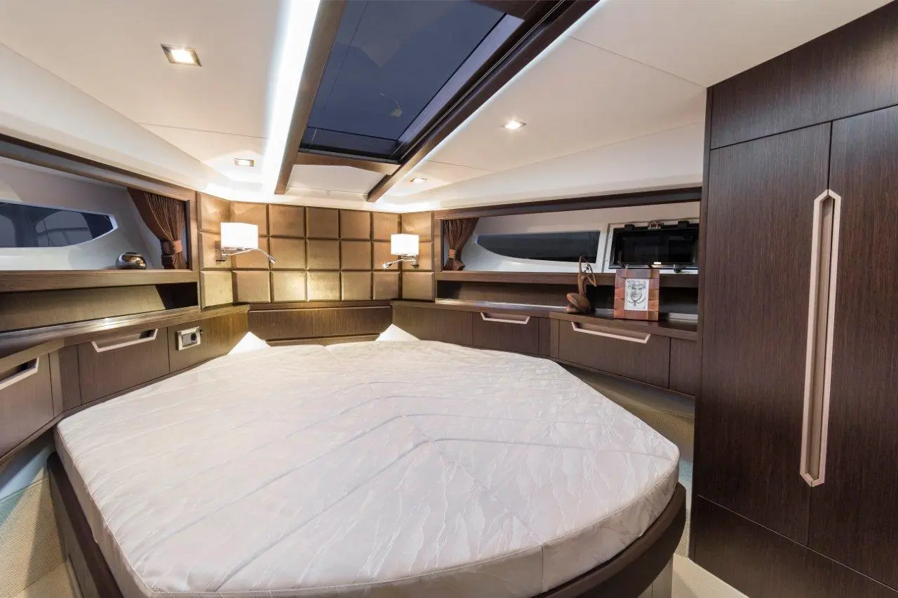 Luxury yacht interior with a round bed, wooden cabinetry, and soft lighting, featuring a skylight and bedside lamps.