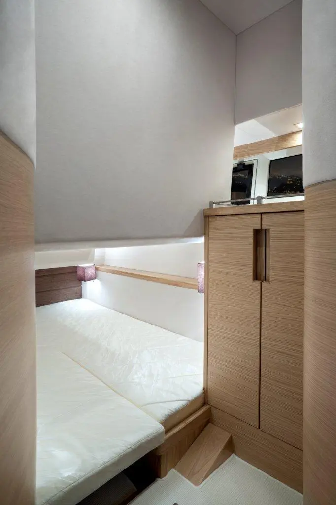 A compact, modern bedroom with a bed, wooden storage cabinet, and soft lighting features in a serene interior setting.