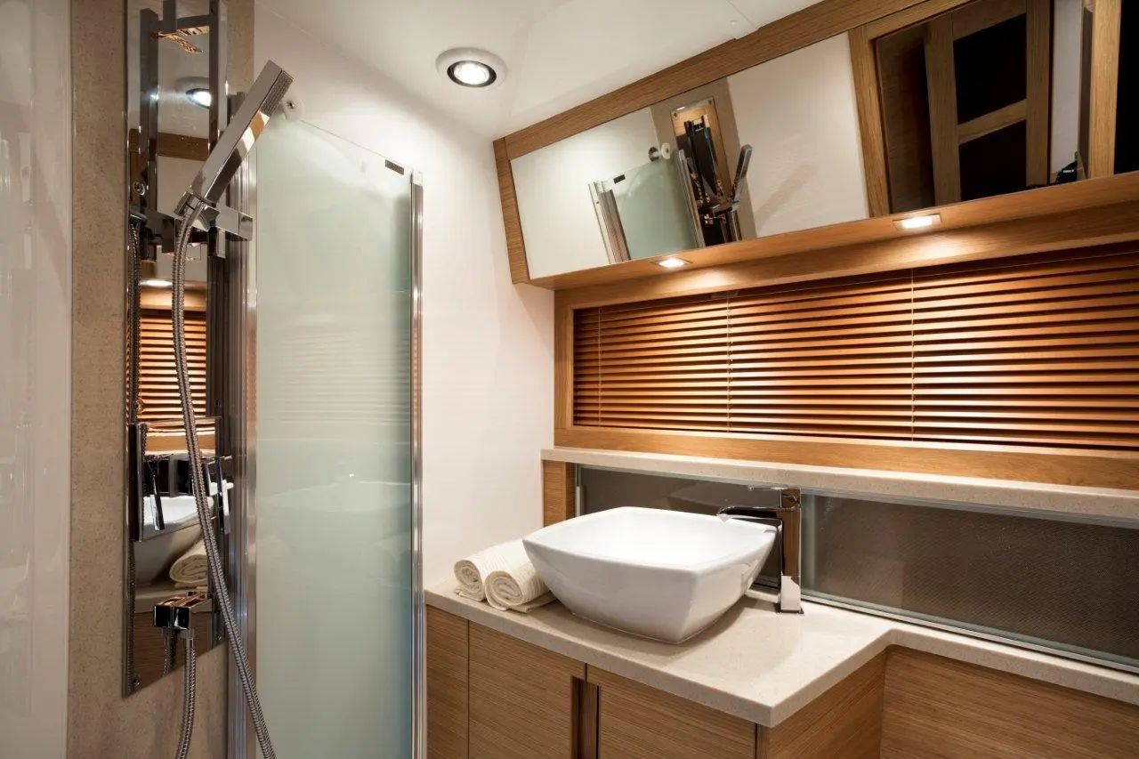 Modern bathroom featuring a glass shower, sleek sink, wooden accents, and stylish lighting. Fresh towels are neatly arranged.