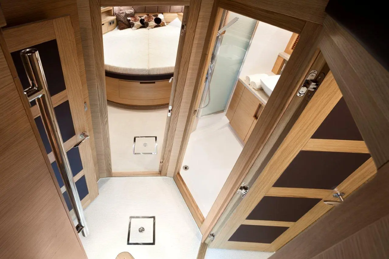 Interior view of a modern yacht bathroom, featuring a shower, wooden cabinetry, and a round bed visible through the doorways.