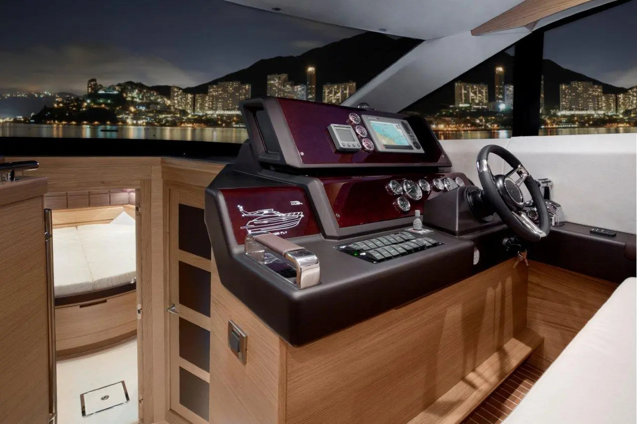 Luxury yacht helm with navigation screens, controls, and city lights reflecting on water at night. Wood finishes enhance elegance.