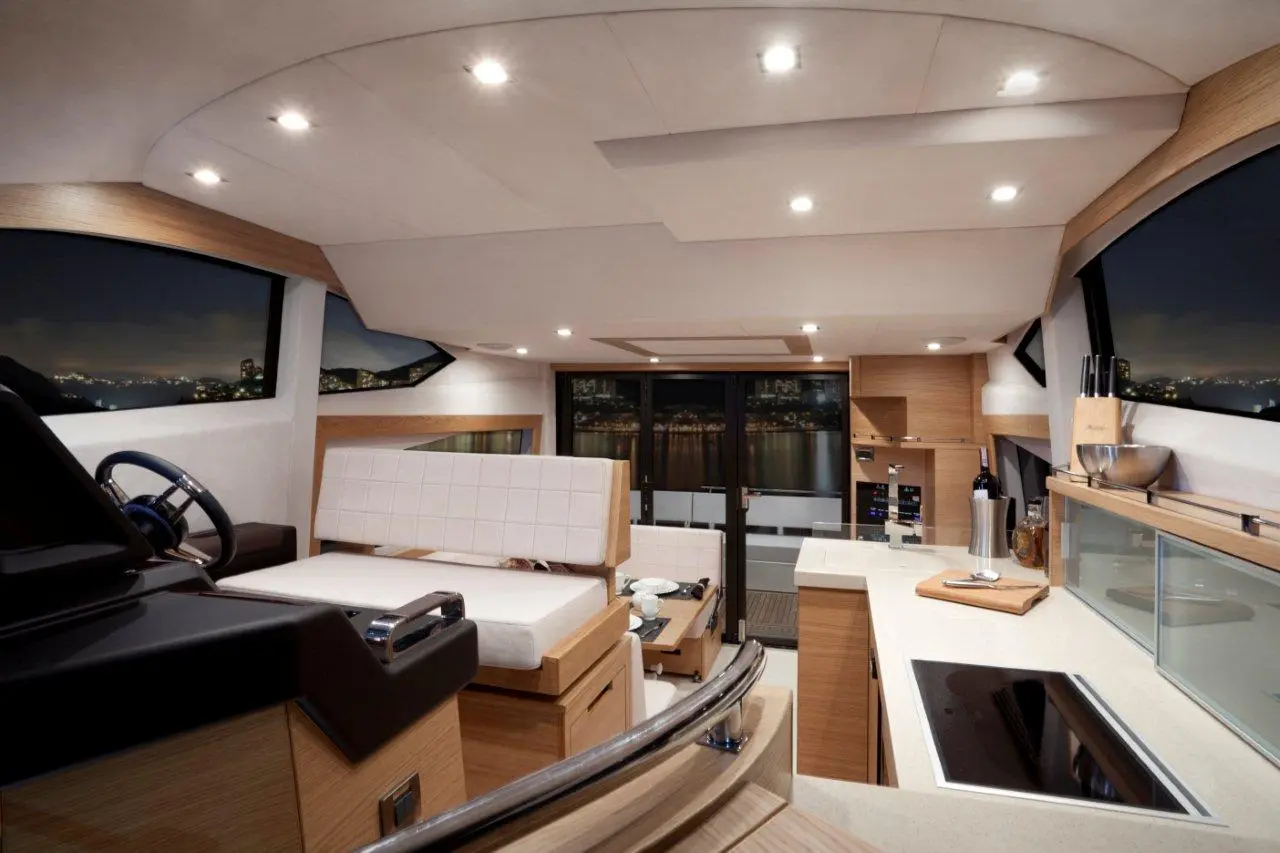 Luxurious boat interior at night with sleek wood finishes, a steering wheel, seating area, and modern kitchen amenities.