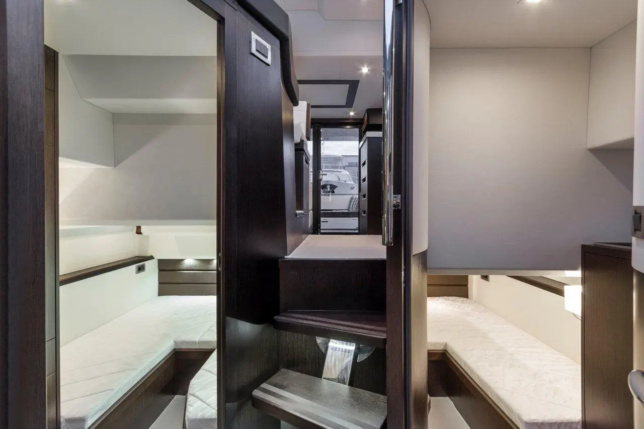 Modern yacht interior featuring a staircase, twin beds, and sleek cabinetry, illuminated by recessed lighting.