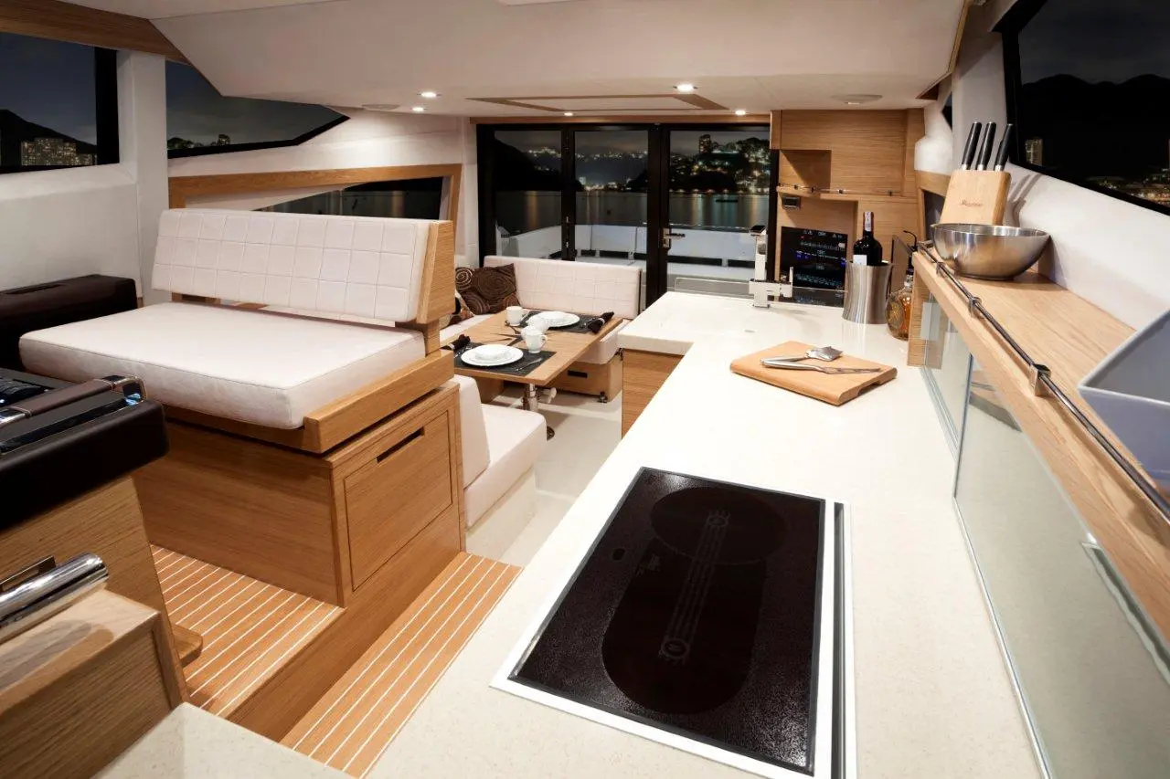 Modern yacht interior featuring a sleek kitchen area, dining space, and large windows showcasing night views.