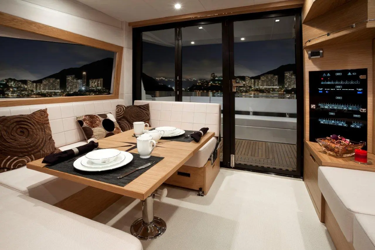 Modern yacht interior featuring a dining table, white decor, plush cushions, and a city skyline view at night.