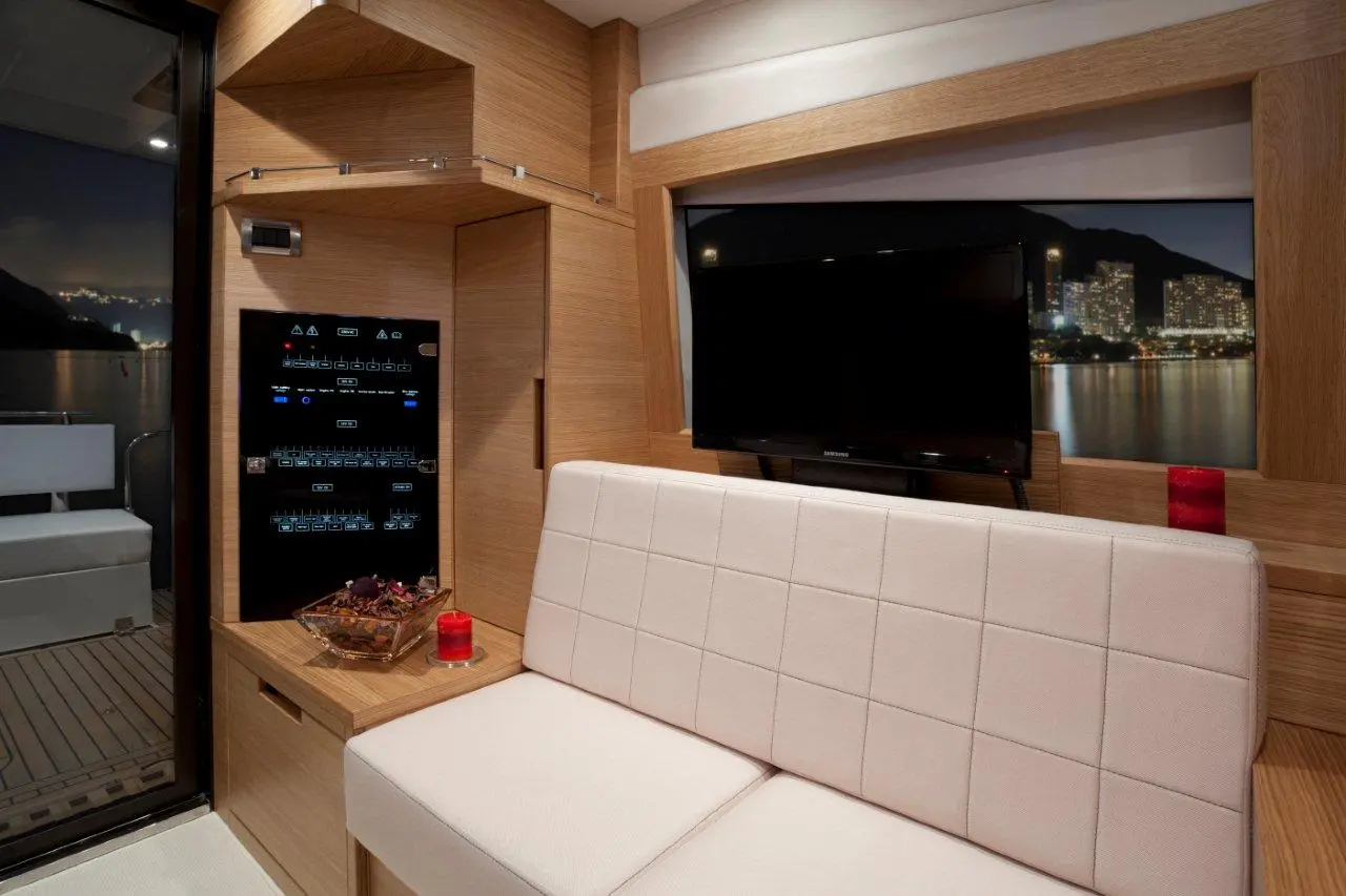 Modern boat interior featuring a white sofa, control panel, TV, and city skyline view through large glass doors.