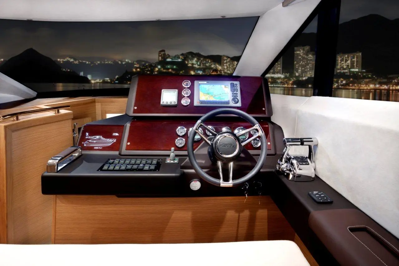 Luxurious yacht cockpit with a wooden dashboard, digital chart plotter, steering wheel, and stunning city view at night.