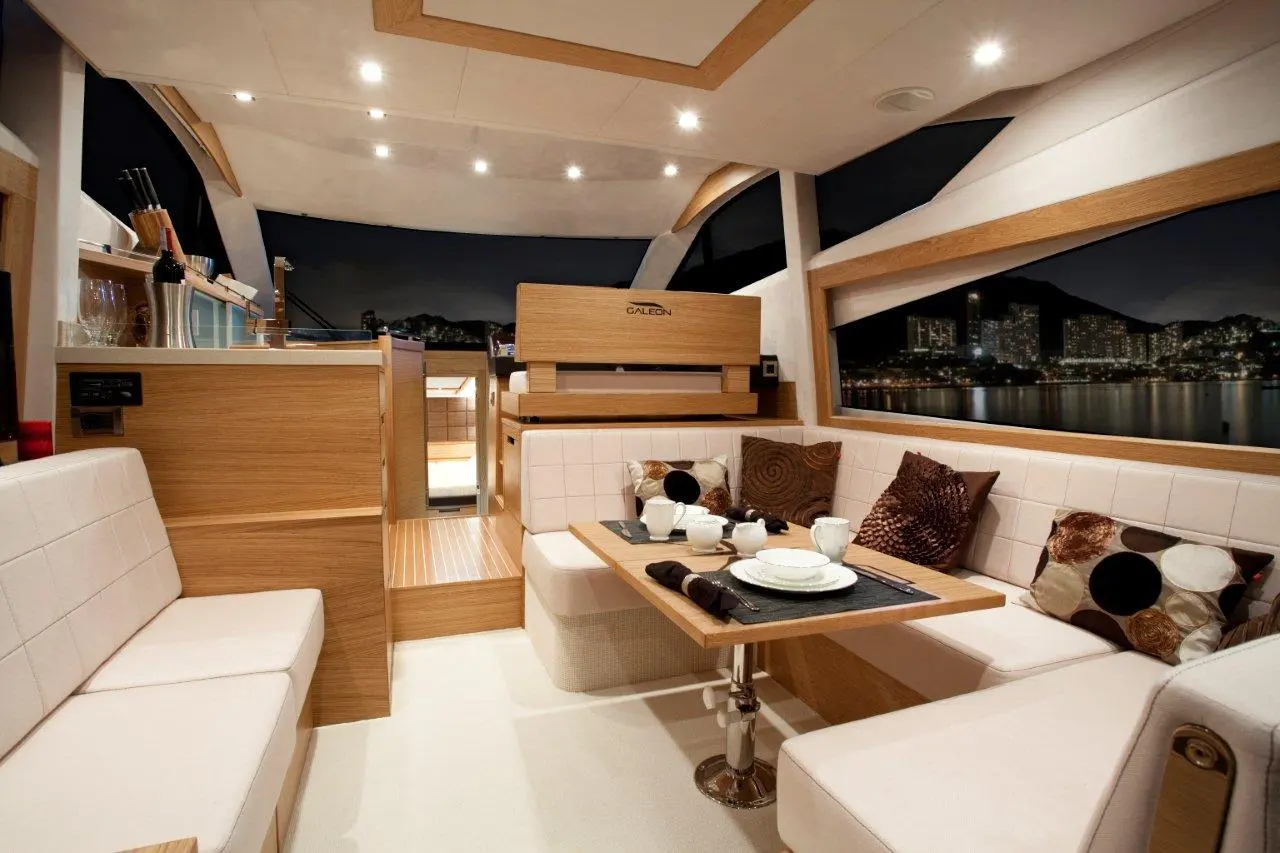 Luxurious yacht interior with wooden accents, a dining area set for tea, and a city skyline visible through large windows.