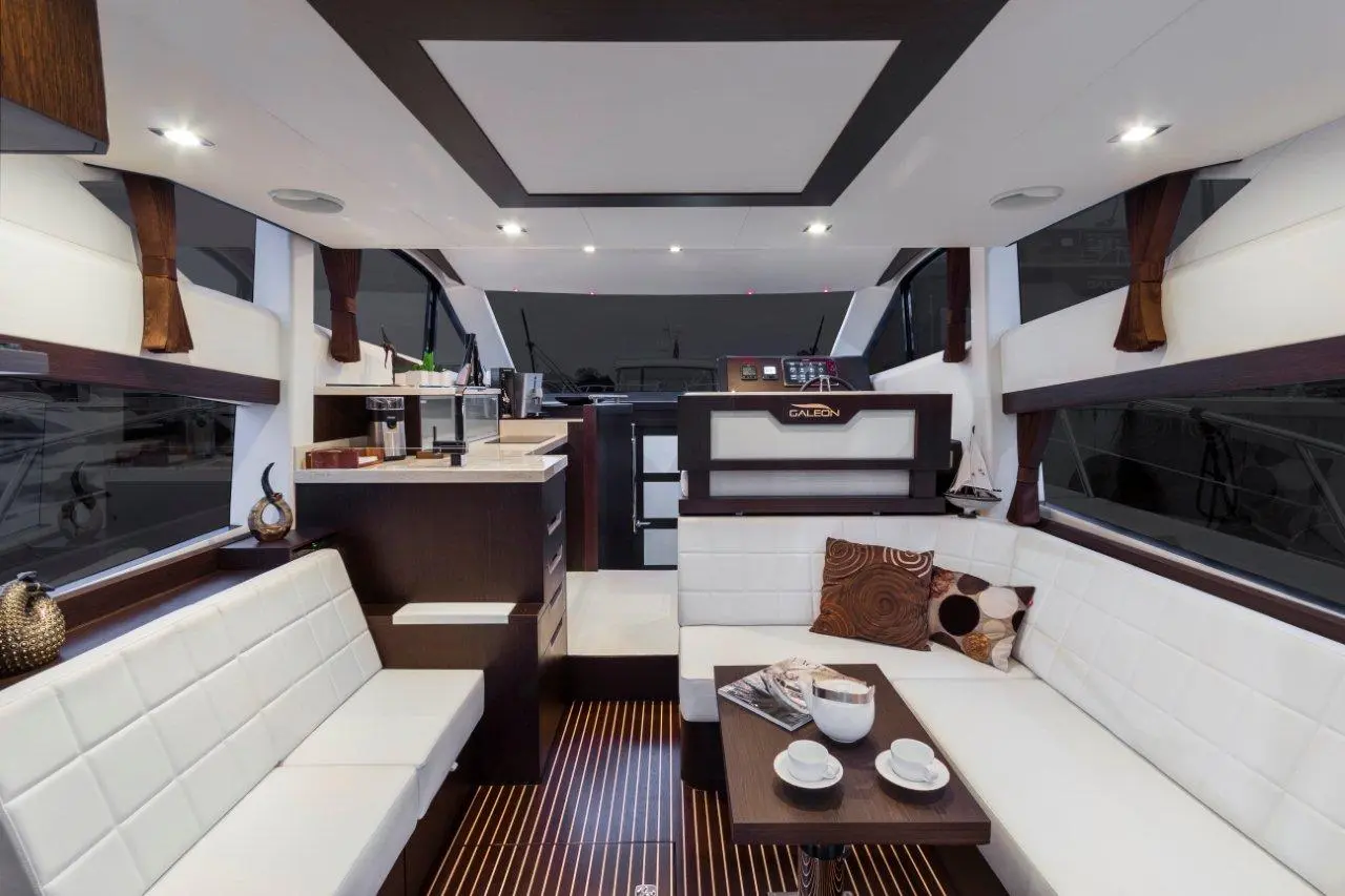 Modern yacht interior featuring white seating, sleek cabinetry, and coffee setup with 'GALEON' branding.