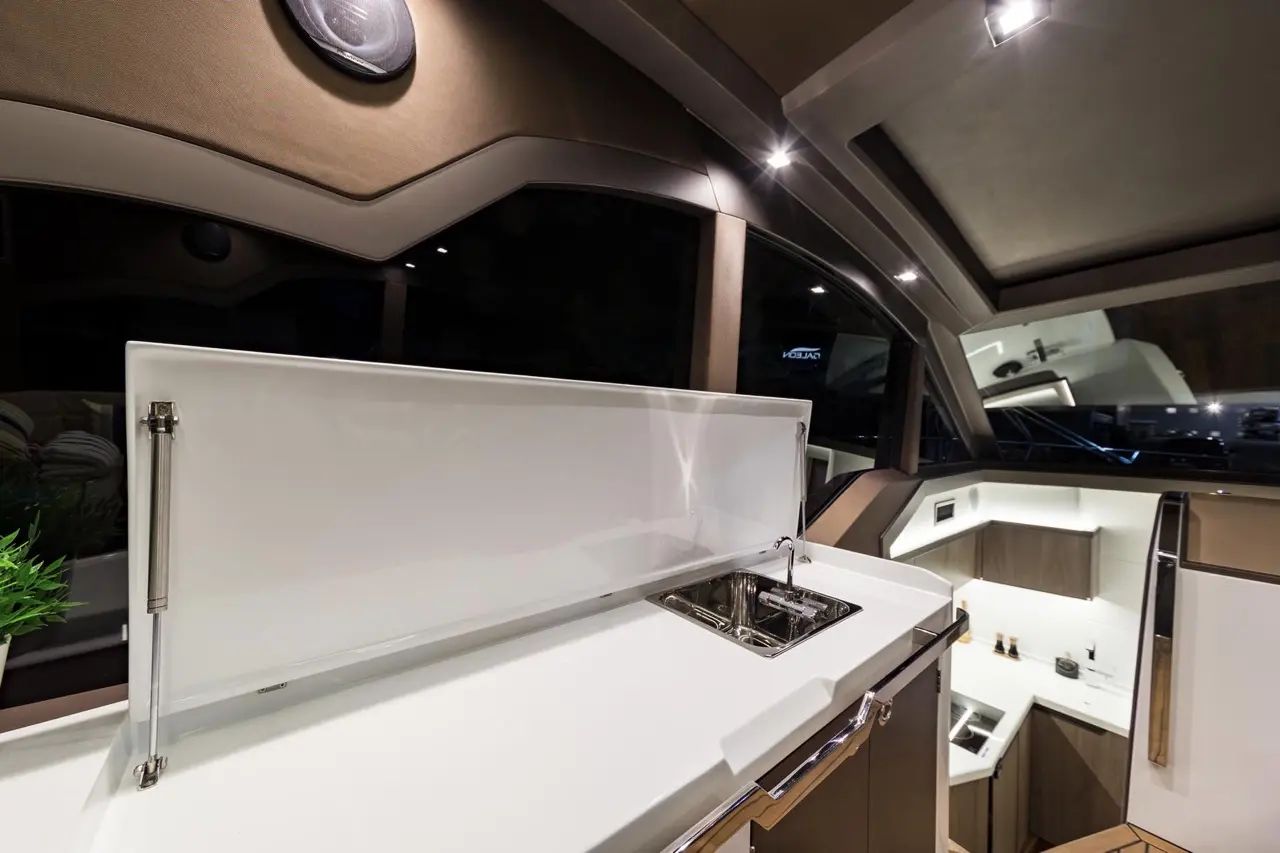 Modern yacht kitchen with a sleek white countertop, sink, and raised backsplash, featuring ambient lighting and cabinetry.
