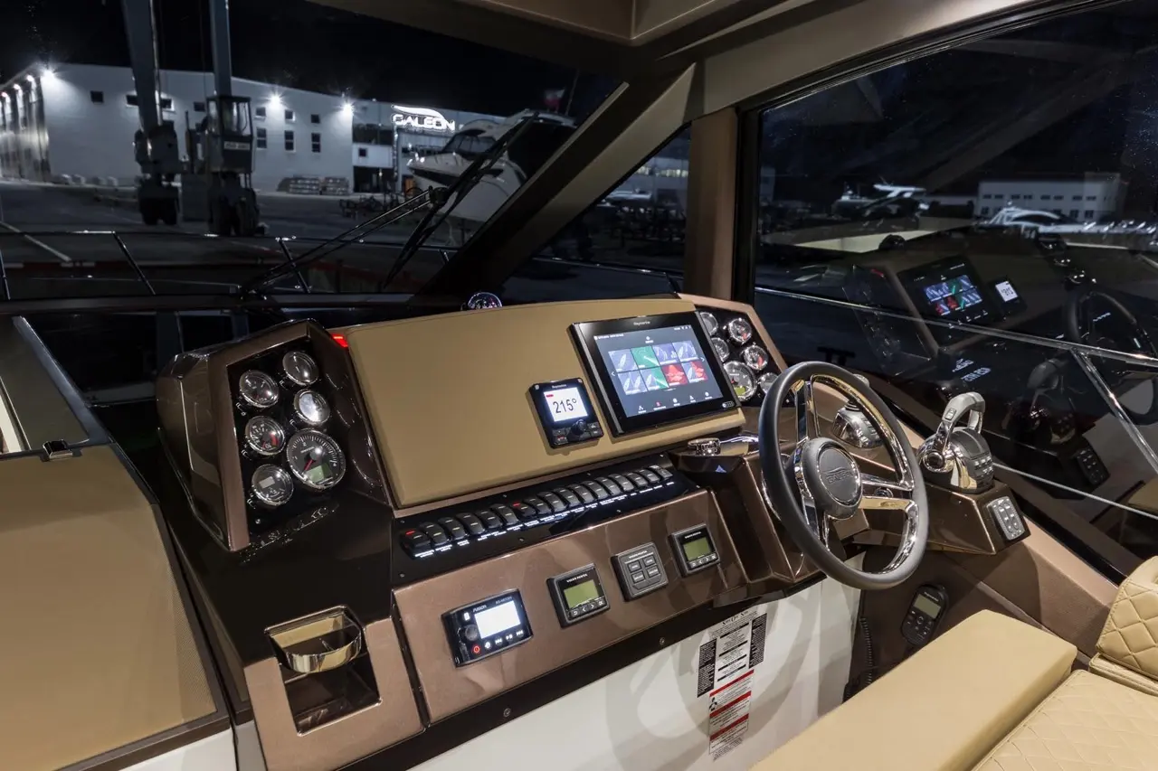 Modern boat cockpit featuring navigation screens, gauges, controls, and a steering wheel, illuminated at night.
