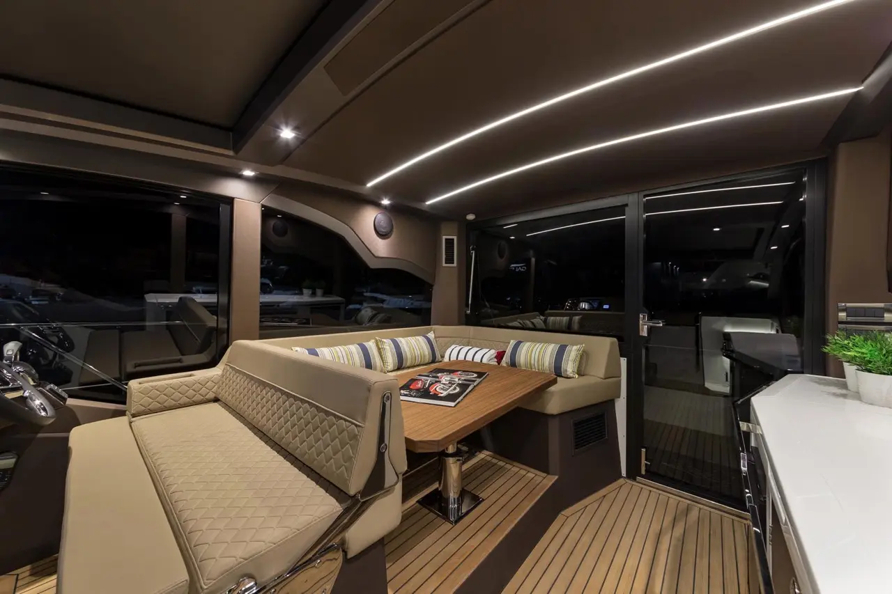Luxurious yacht interior featuring a plush sofa, dining table, modern lighting, and large windows with a nighttime view.