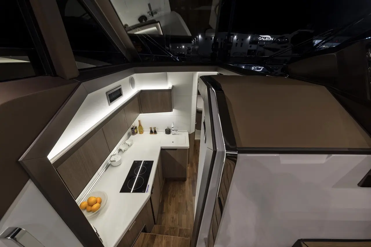 Modern yacht kitchen featuring sleek cabinetry, a stove, and countertop with a fruit bowl, illuminated by stylish lighting.