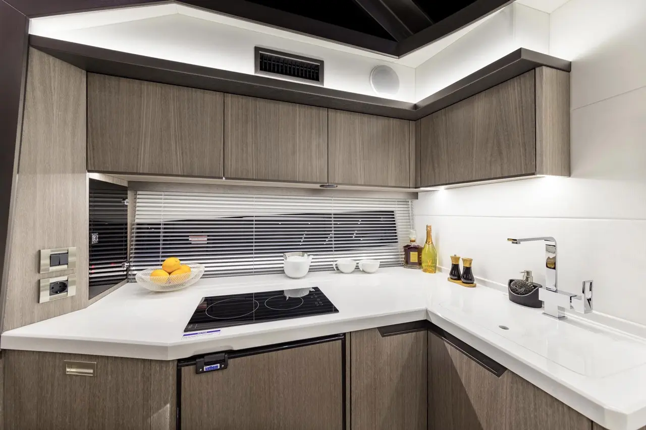 Modern kitchen with sleek gray cabinetry, a white countertop, stove, sink, yellow lemons in a bowl, and decorative bottles.