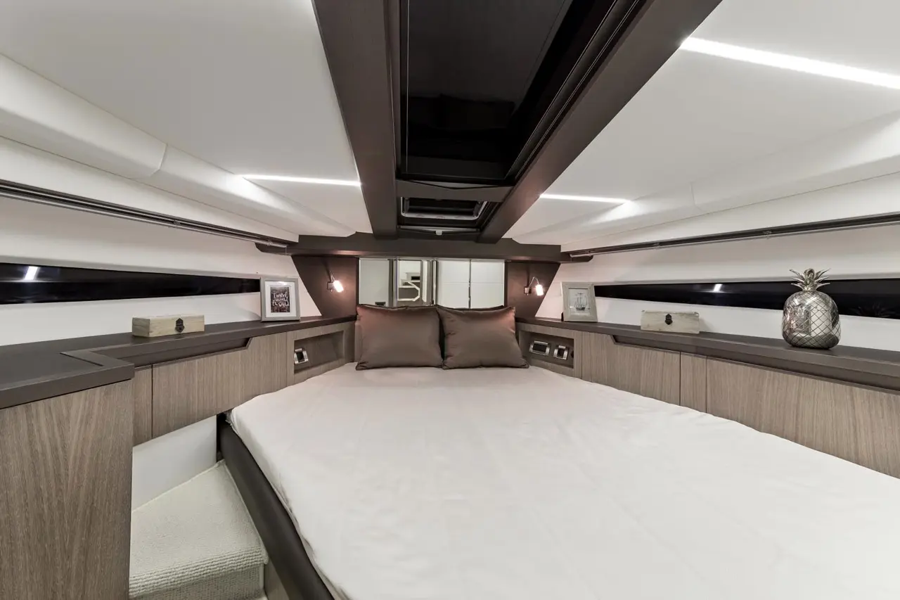 Modern yacht interior featuring a cozy bed, brown pillows, decorative accents, and ambient lighting in wood and white finishes.