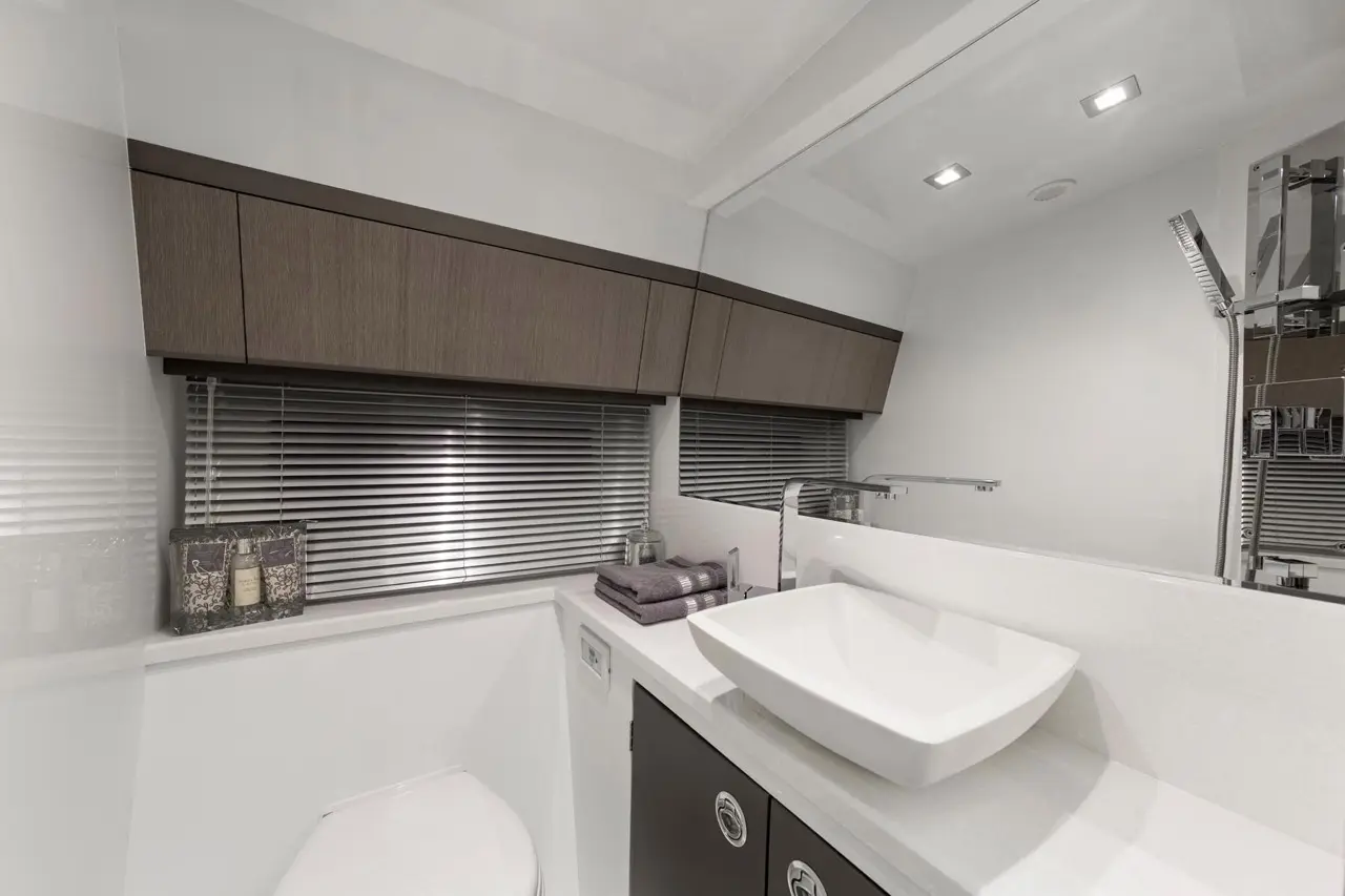 Modern bathroom interior featuring a white sink, gray towels, and wooden cabinetry with a large mirror and blinds.
