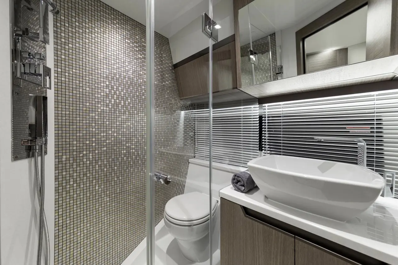 Modern bathroom featuring a glass shower, a sleek toilet, elegant mosaic tiles, and a stylish bowl sink with a towel.