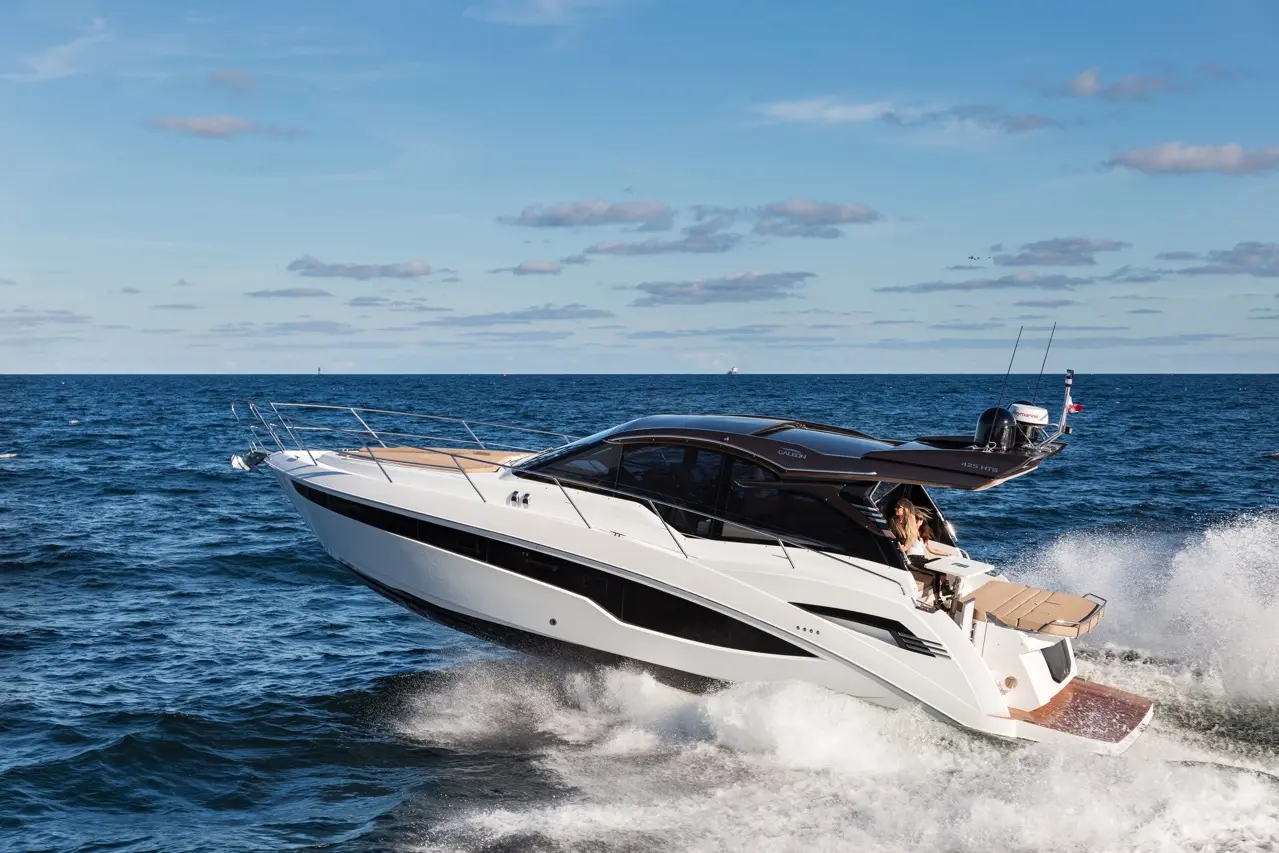 Luxury powerboat jumping over waves with a woman at the helm, blue sky and ocean in the background.