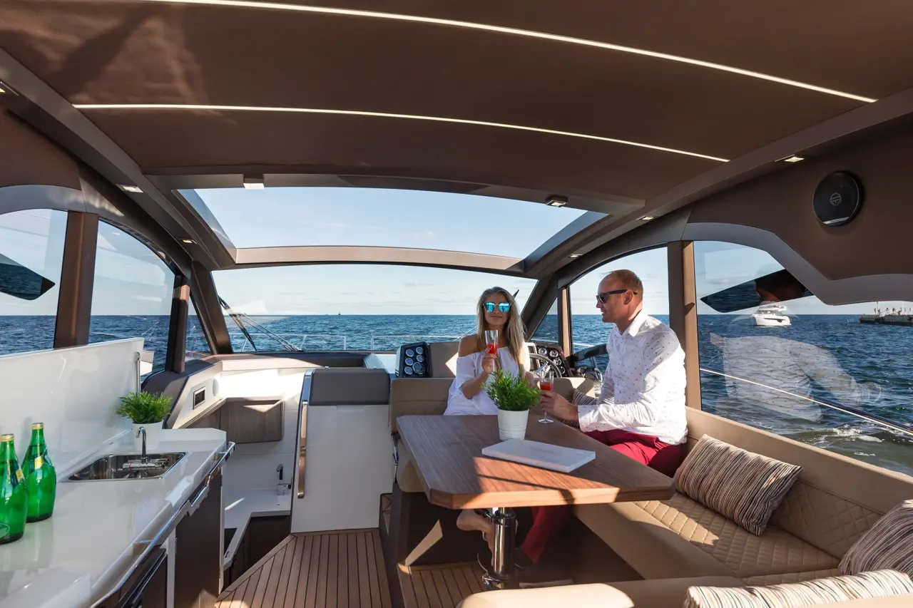 A couple enjoys drinks on a luxury yacht's interior, featuring a modern design, ocean views, and a stylish dining area.