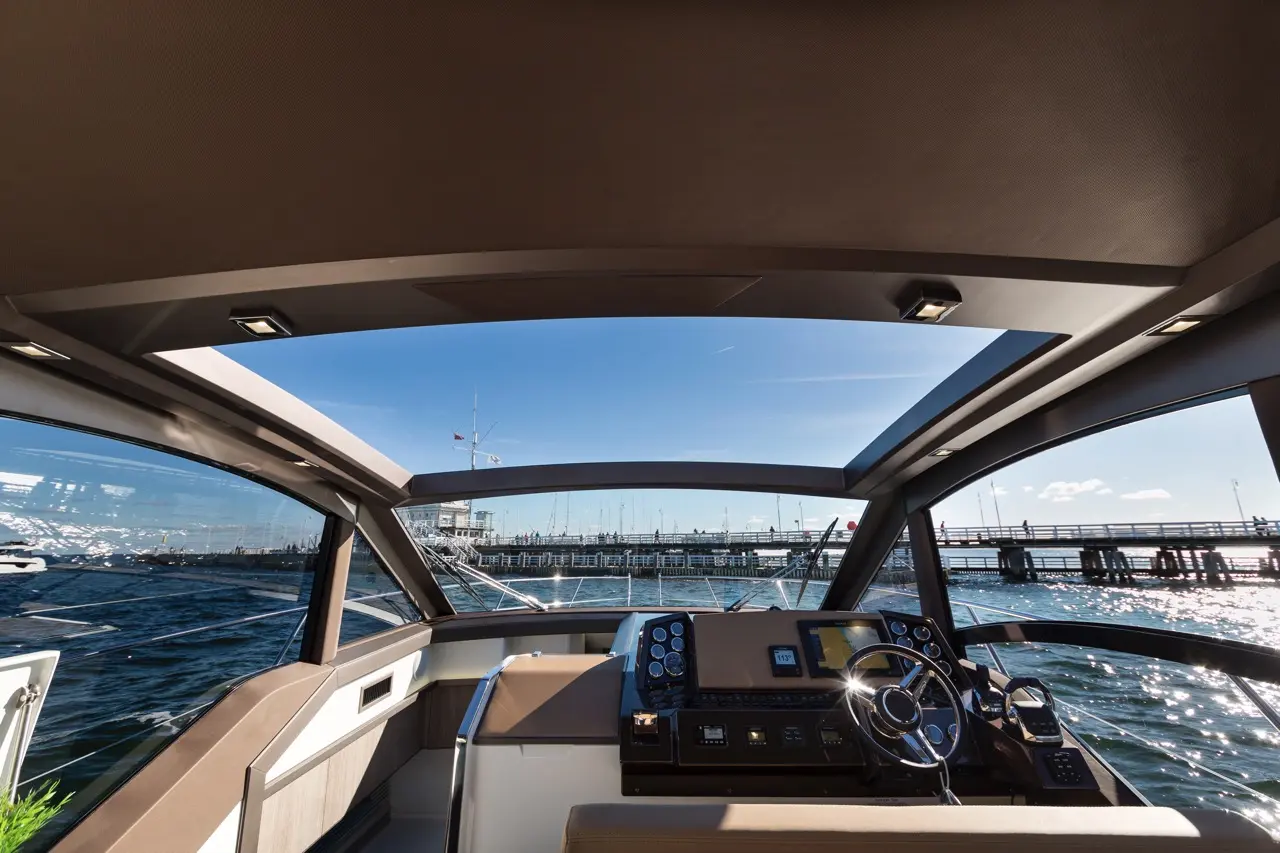 Luxurious boat cockpit with modern controls, panoramic view of marina under clear blue sky and sunlight reflecting on water.
