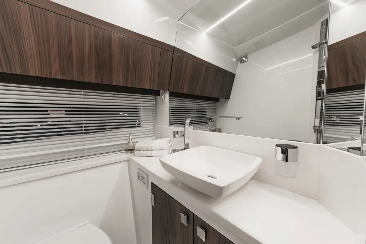 Modern bathroom with a white basin, wooden cabinetry, fresh towels, and a large mirror illuminated by indirect lighting.