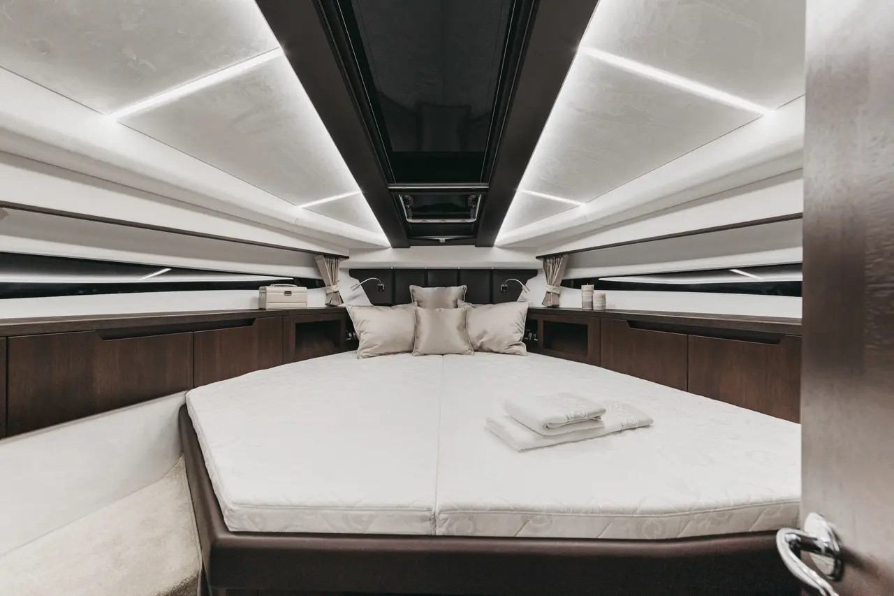 Luxurious boat interior featuring a large bed with cushions, soft lighting, and elegant cabinetry, creating a serene atmosphere.