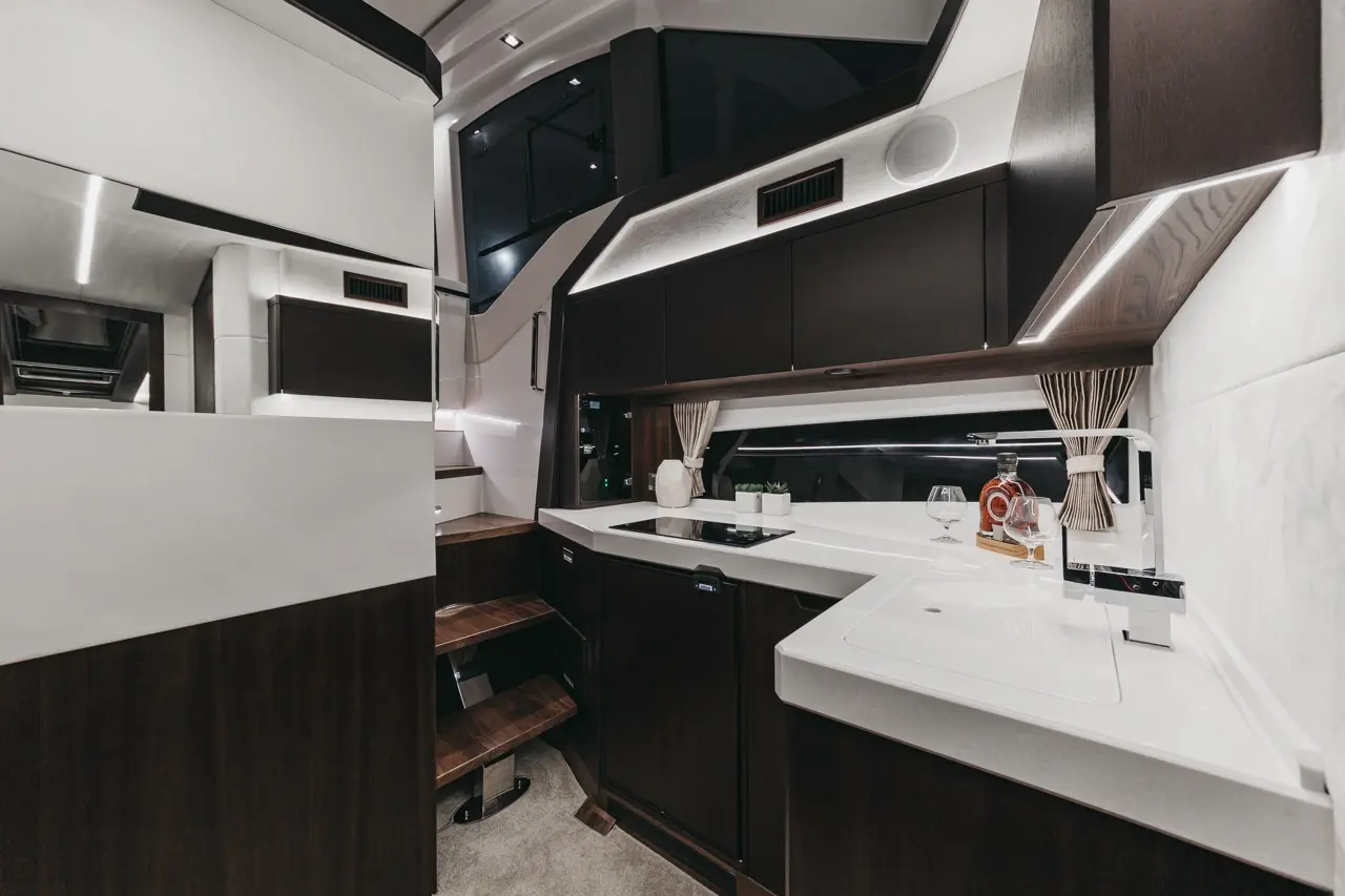 Modern kitchen interior featuring dark cabinetry, marble countertops, and glassware on display, illuminated by ambient lighting.