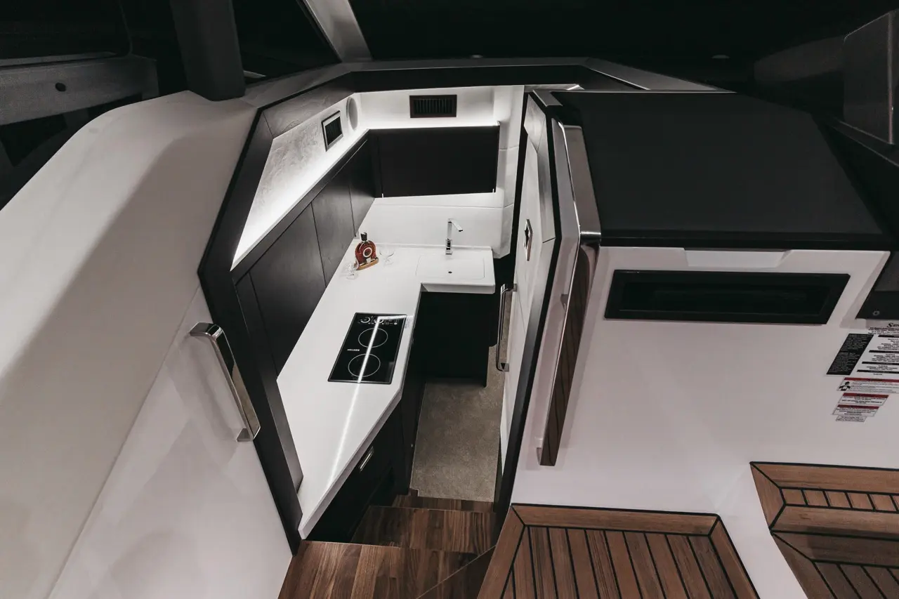 Modern yacht kitchen featuring black cabinetry, white countertops, stovetop, sink, and a decorative bottle with glasses.