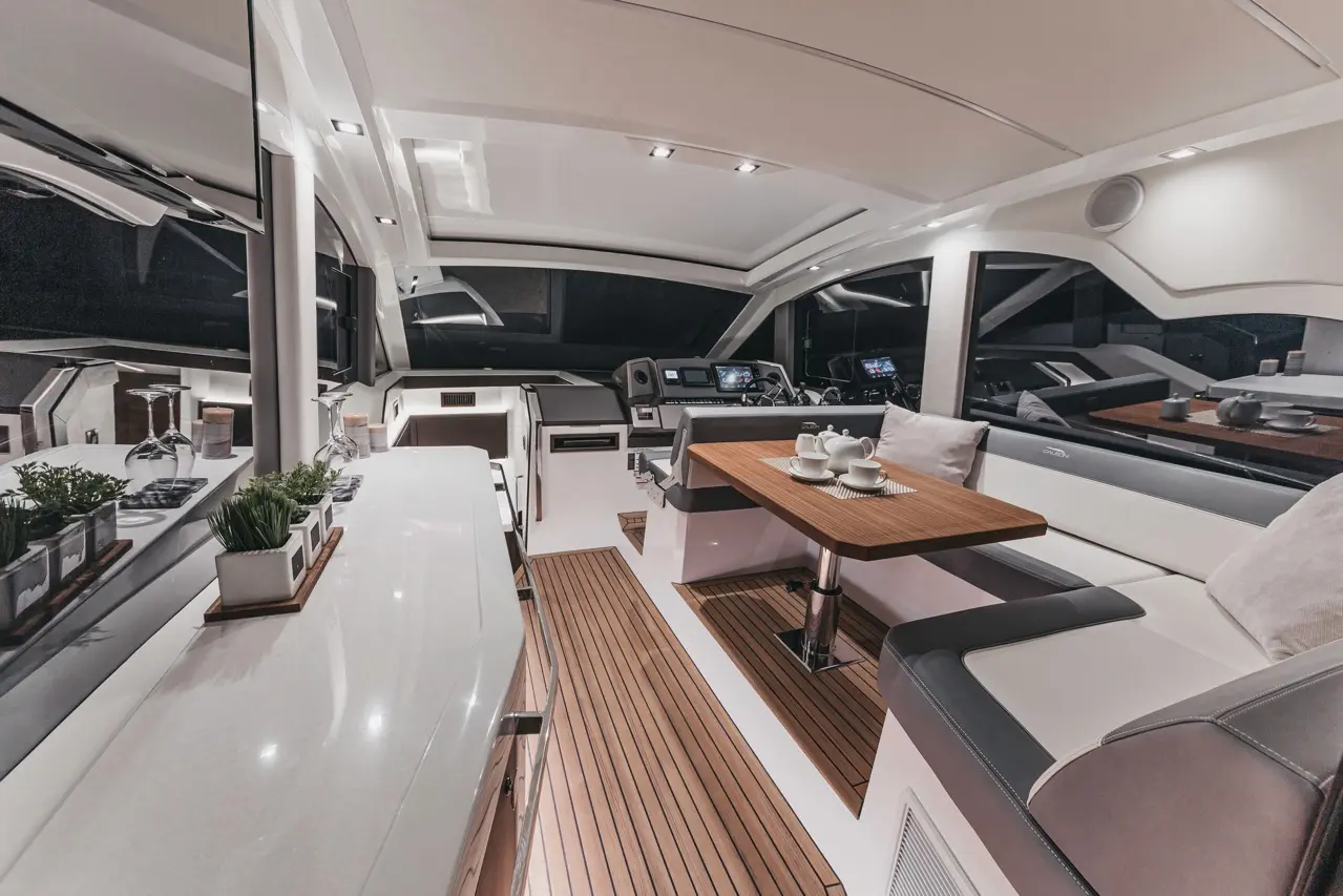 Modern yacht interior with a sleek design, featuring a dining area, steering console, and decorative plants.