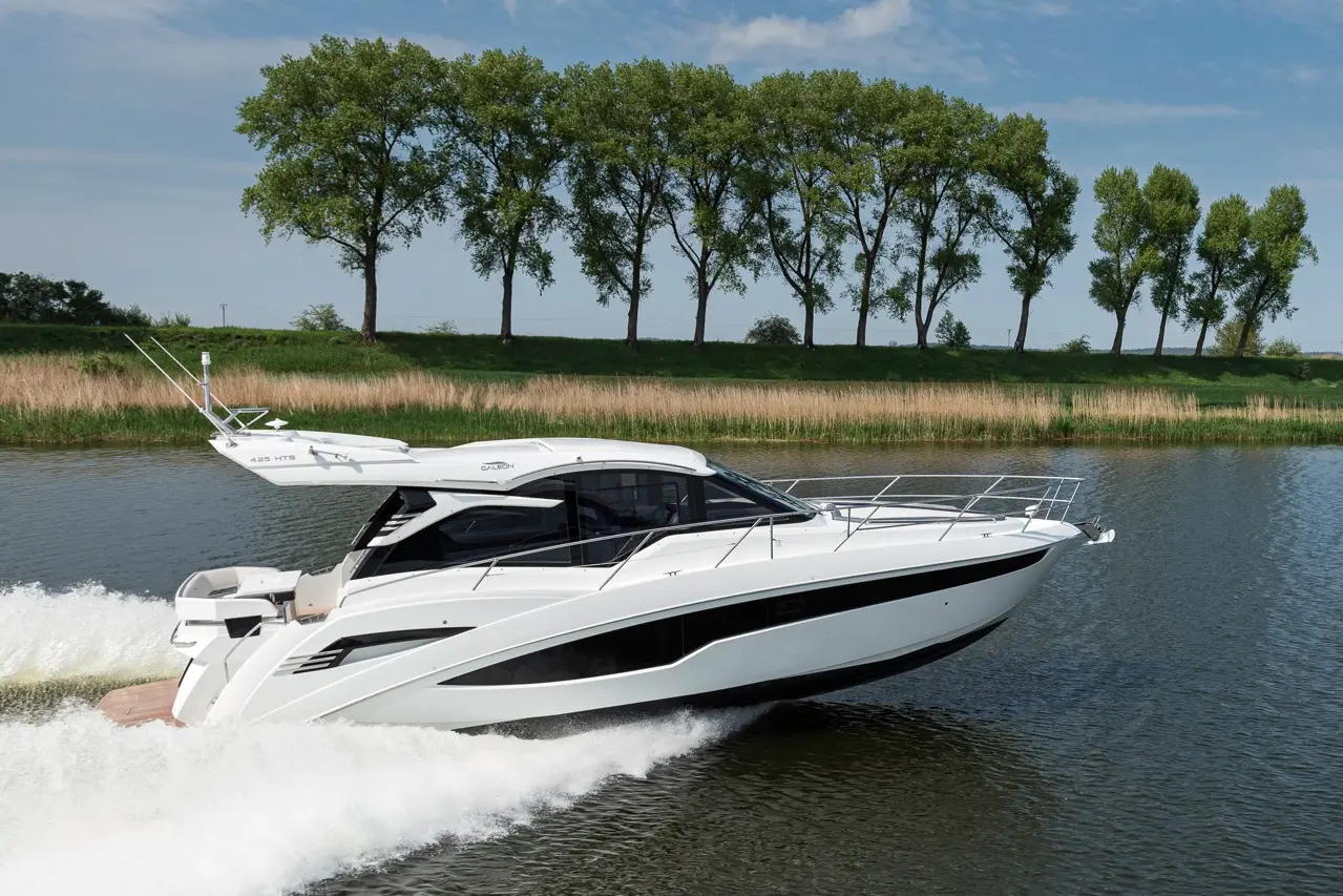 A sleek white motorboat, cruising at speed on a calm river, surrounded by green trees and tall grass.