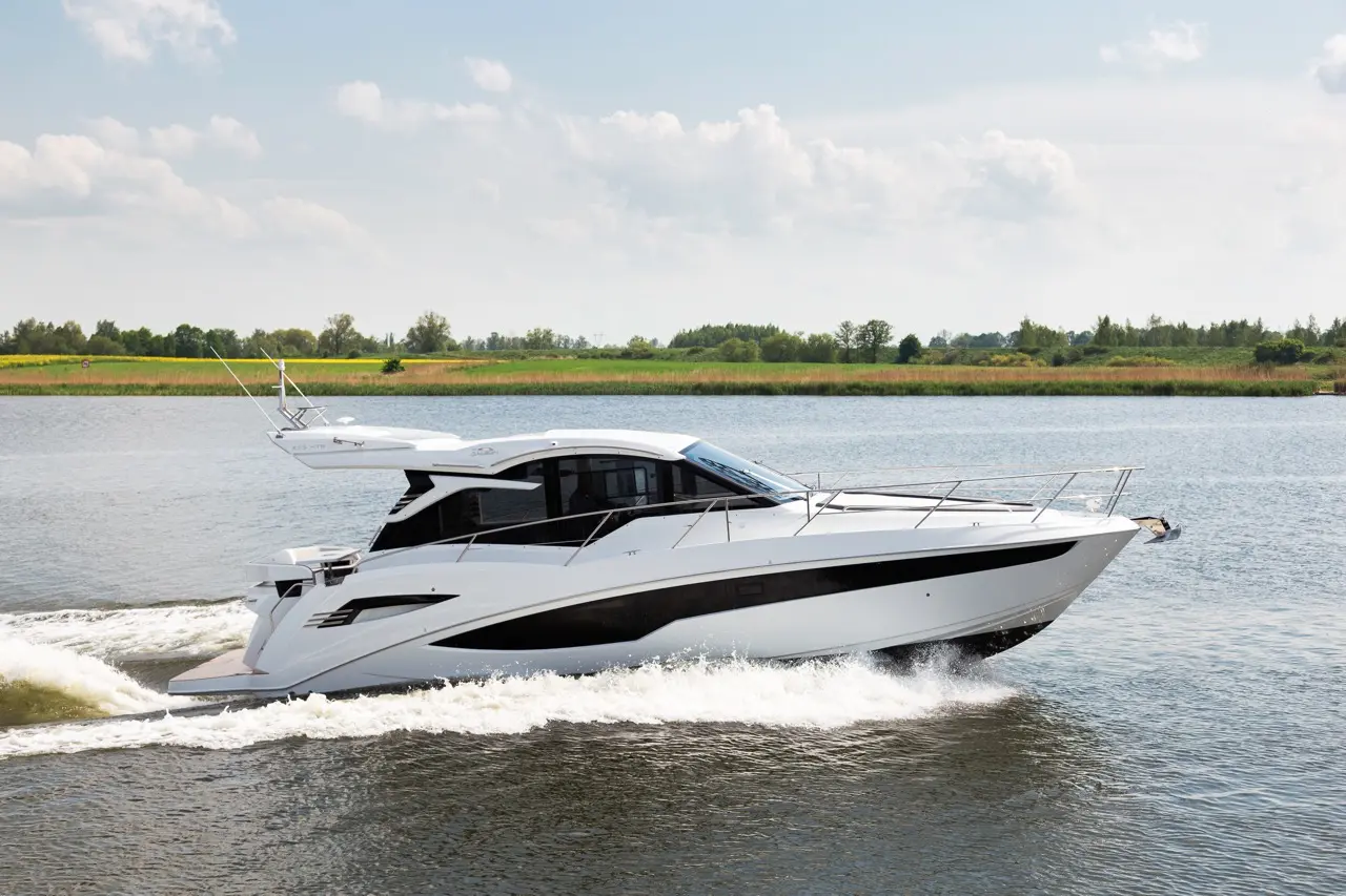 Luxury motor yacht gliding through calm water, surrounded by green landscape and clear blue sky, creating a serene atmosphere.