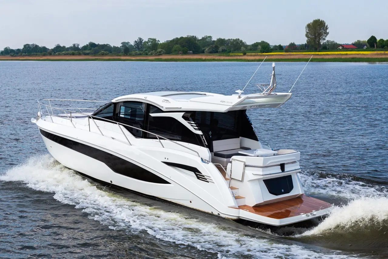 A sleek white and black motorboat, model 425 HYB, glides on calm water surrounded by greenery and a clear sky.