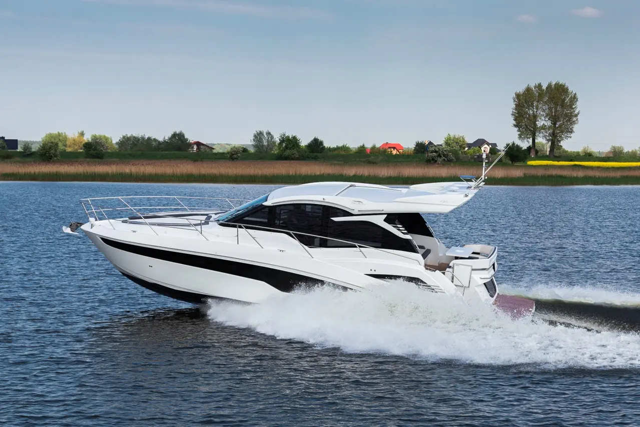 A sleek white motorboat glides across calm waters, leaving a spray in its wake against a lush green landscape.