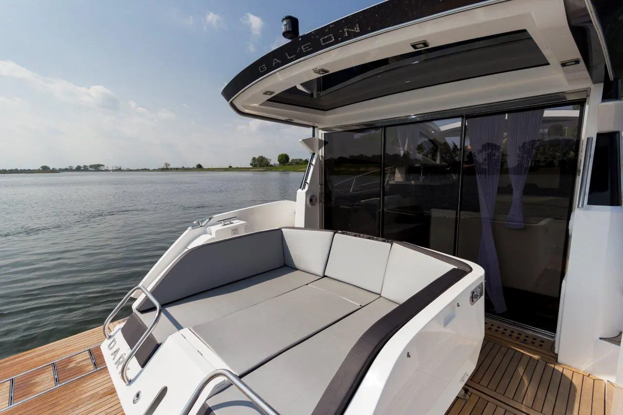 Luxury boat deck featuring a spacious gray seating area, with a view of calm water and a sunny sky.