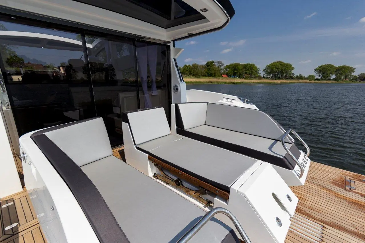 Modern boat deck featuring two gray cushioned seats and a retractable table, overlooking calm water and greenery.